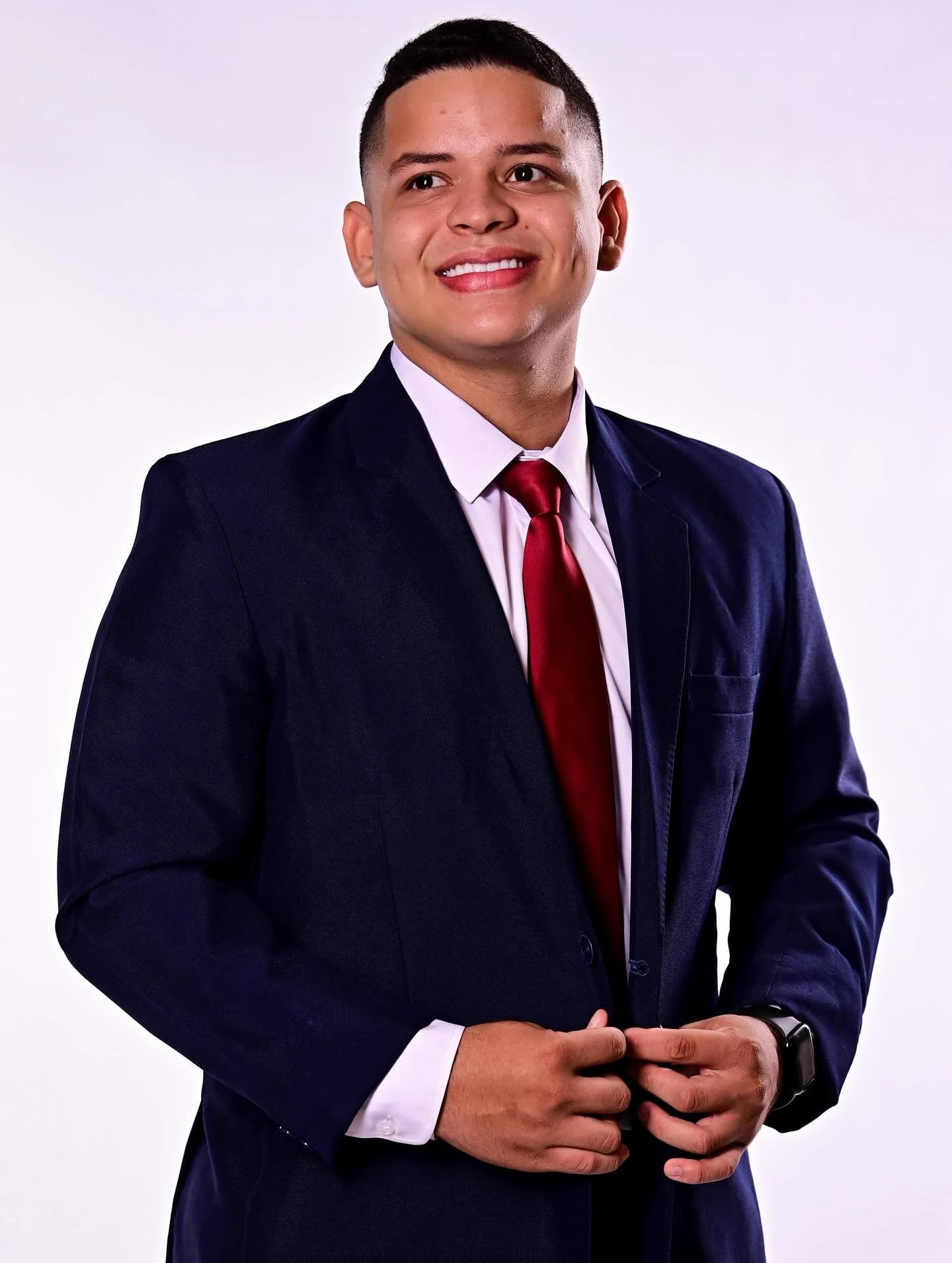 Eric Ferraz em pose levemente de lado, vestindo terno azul-marinho e gravata vermelha.
